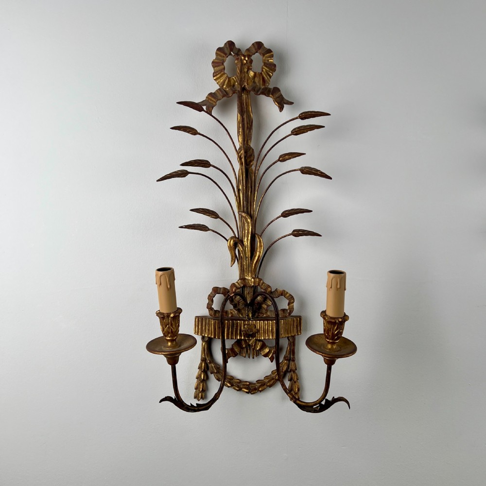 A pair of early 20th-century Italian giltwood and toleware wall sconces featuring carved ribbon bow crests, rising foliage sprigs, and twin candle arms. View V