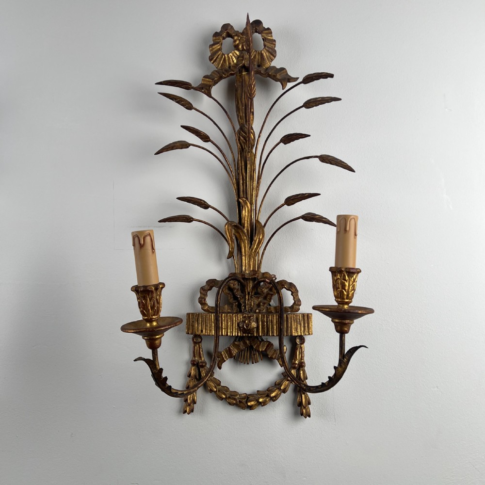A pair of early 20th-century Italian giltwood and toleware wall sconces featuring carved ribbon bow crests, rising foliage sprigs, and twin candle arms. View VI