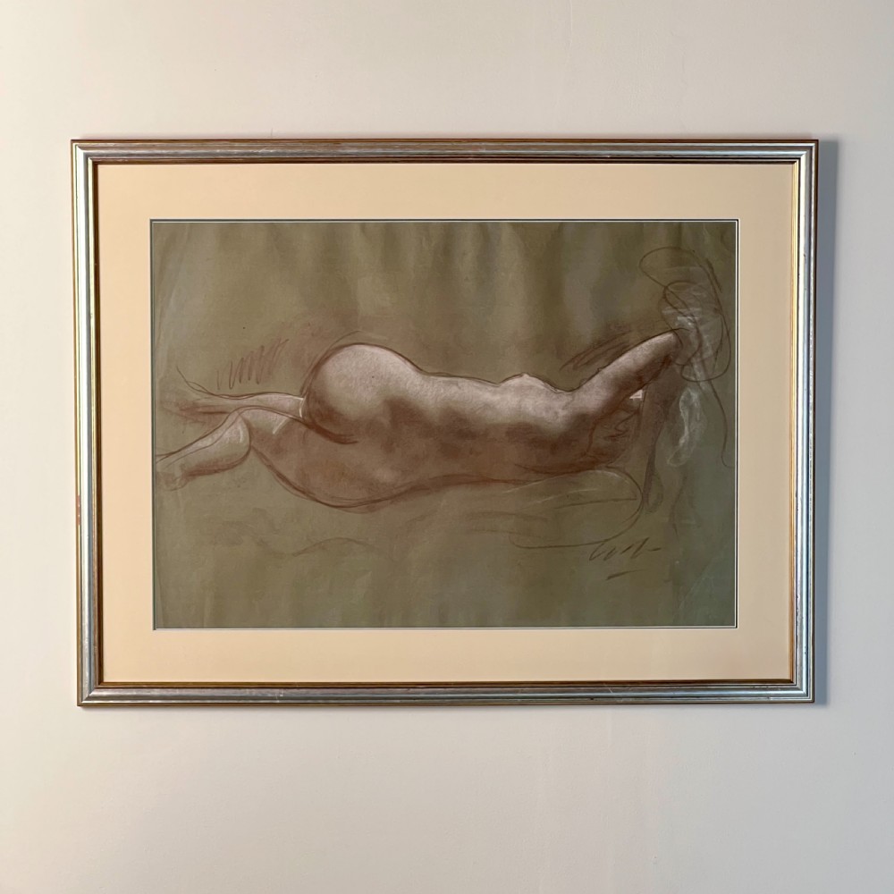 A framed charcoal and chalk life study drawing depicting a reclining female nude figure on toned paper.