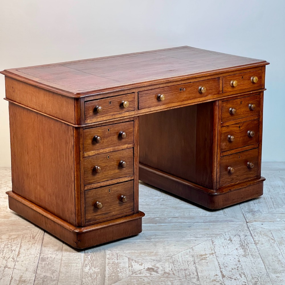 An antique Victorian oak pedestal desk featuring nine drawers with turned wooden knobs and a leather writing surface on twin plinth bases.