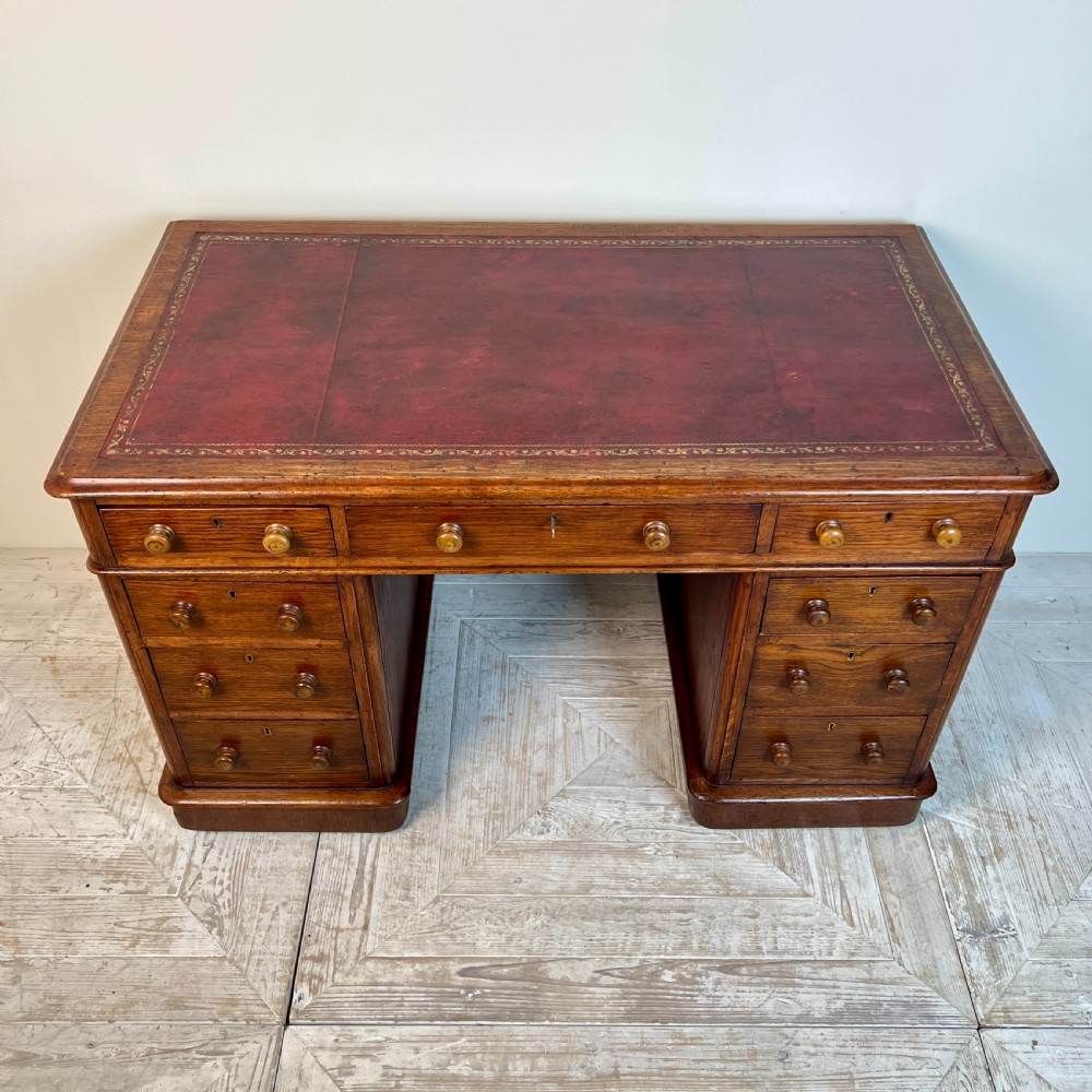 An antique Victorian oak pedestal desk featuring nine drawers with turned wooden knobs and a leather writing surface on twin plinth bases. View II