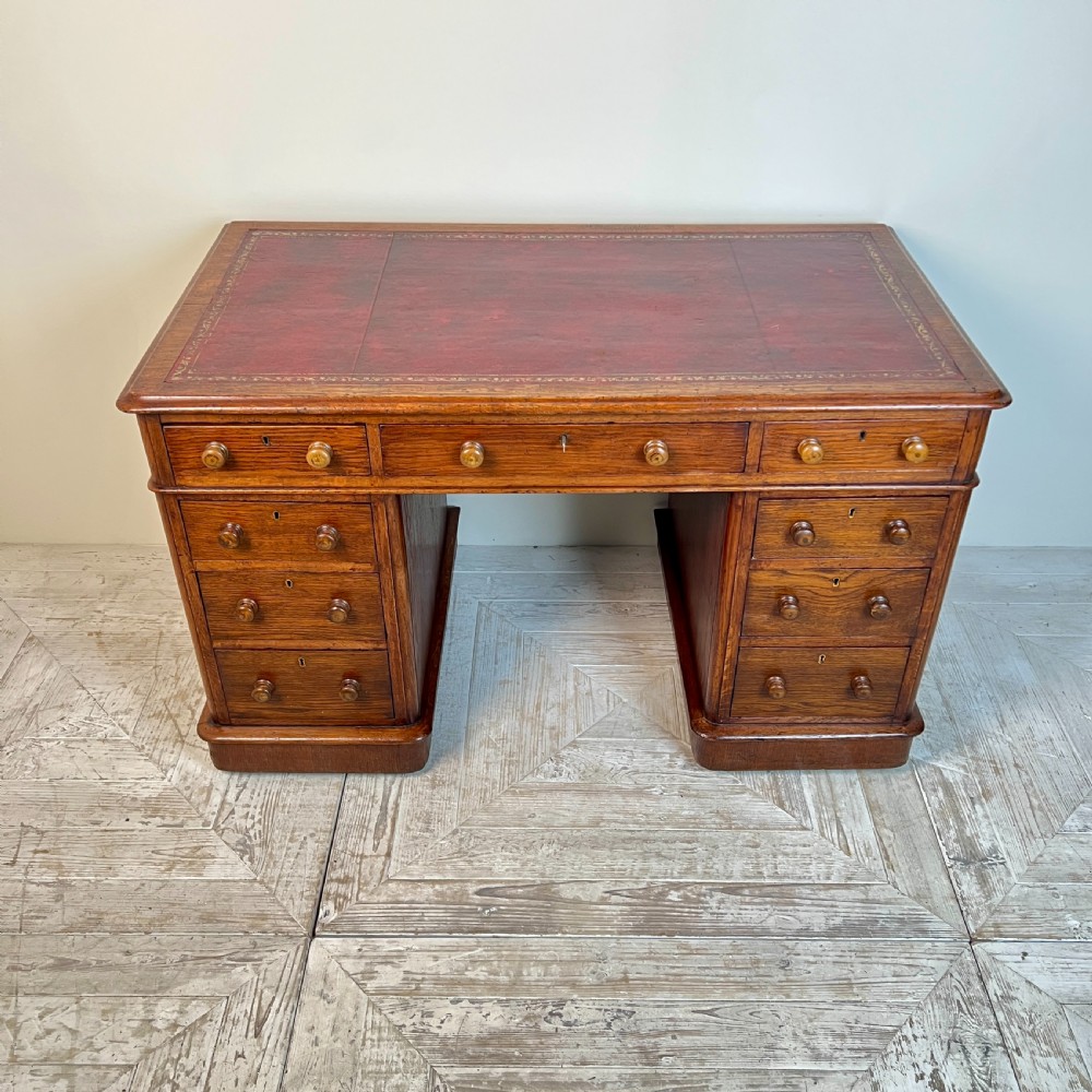 An antique Victorian oak pedestal desk featuring nine drawers with turned wooden knobs and a leather writing surface on twin plinth bases. View III