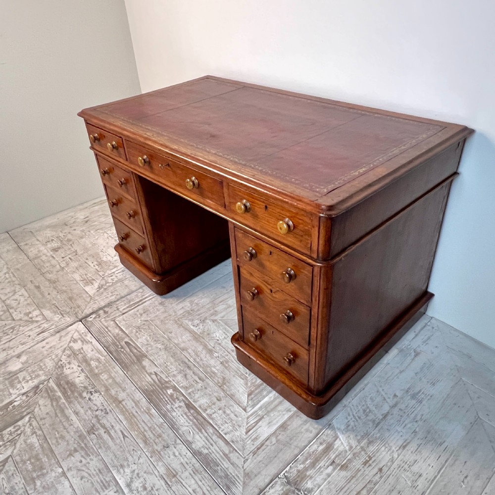 An antique Victorian oak pedestal desk featuring nine drawers with turned wooden knobs and a leather writing surface on twin plinth bases. View V