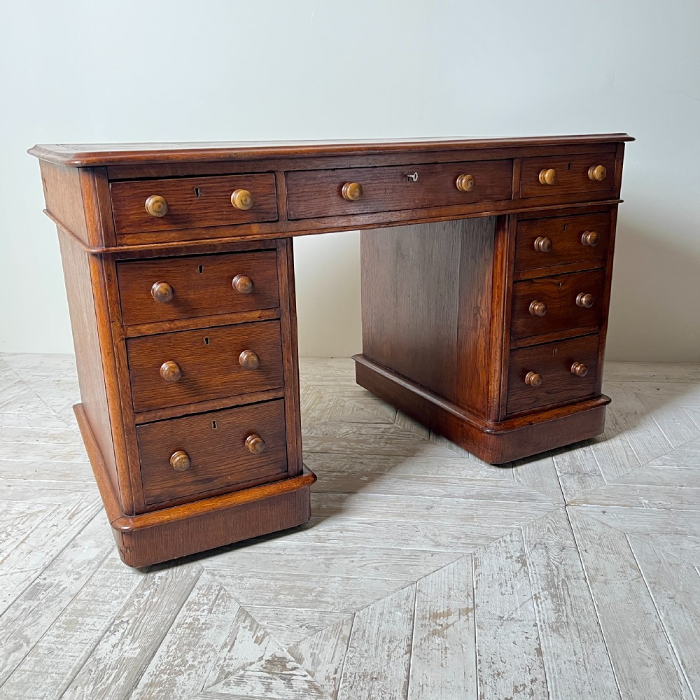 An antique Victorian oak pedestal desk featuring nine drawers with turned wooden knobs and a leather writing surface on twin plinth bases. View VII