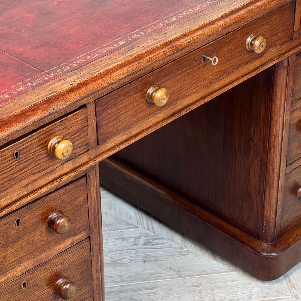 An antique Victorian oak pedestal desk featuring nine drawers with turned wooden knobs and a leather writing surface on twin plinth bases. View VIII
