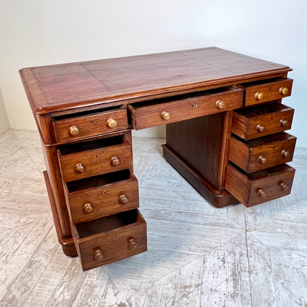 An antique Victorian oak pedestal desk featuring nine drawers with turned wooden knobs and a leather writing surface on twin plinth bases. View IX