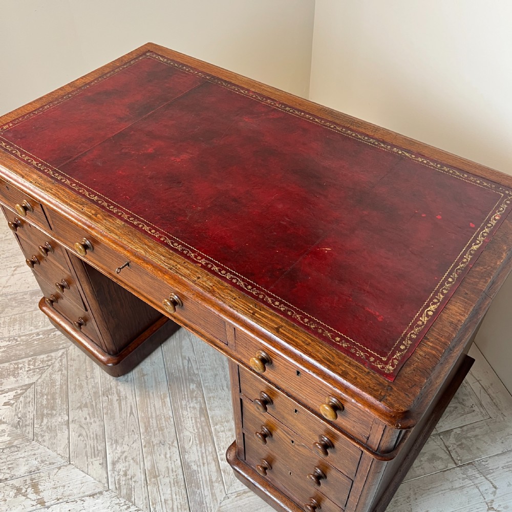 An antique Victorian oak pedestal desk featuring nine drawers with turned wooden knobs and a leather writing surface on twin plinth bases. View X