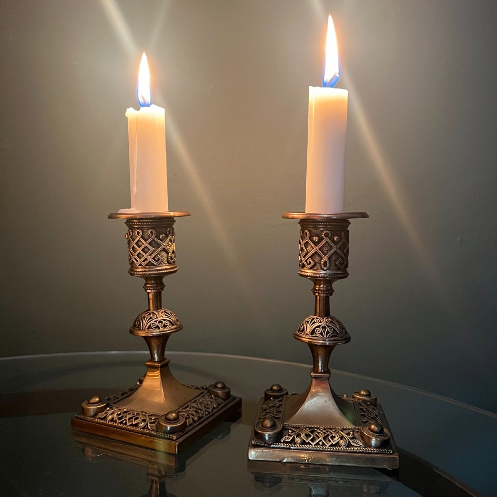 A pair of late Victorian Aesthetic Movement cast brass candlesticks featuring square bases and cylindrical sconces decorated with geometric fretwork. View VII