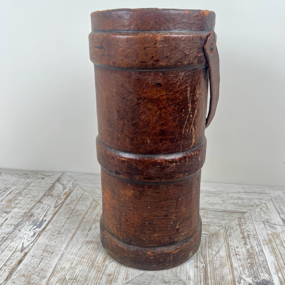 A tall cylindrical brown leather First World War artillery shell carrier featuring heavy stitched seams and a riveted side handle.