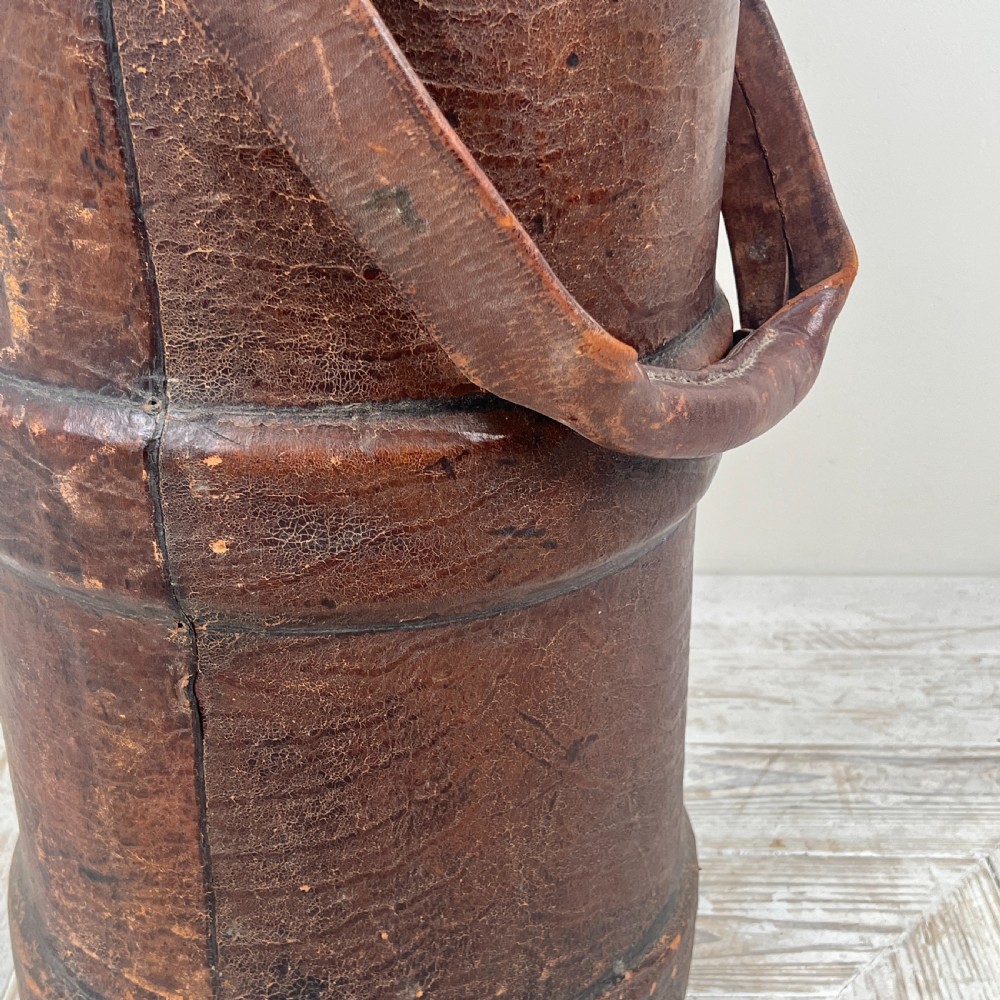 A tall cylindrical brown leather First World War artillery shell carrier featuring heavy stitched seams and a riveted side handle. View III