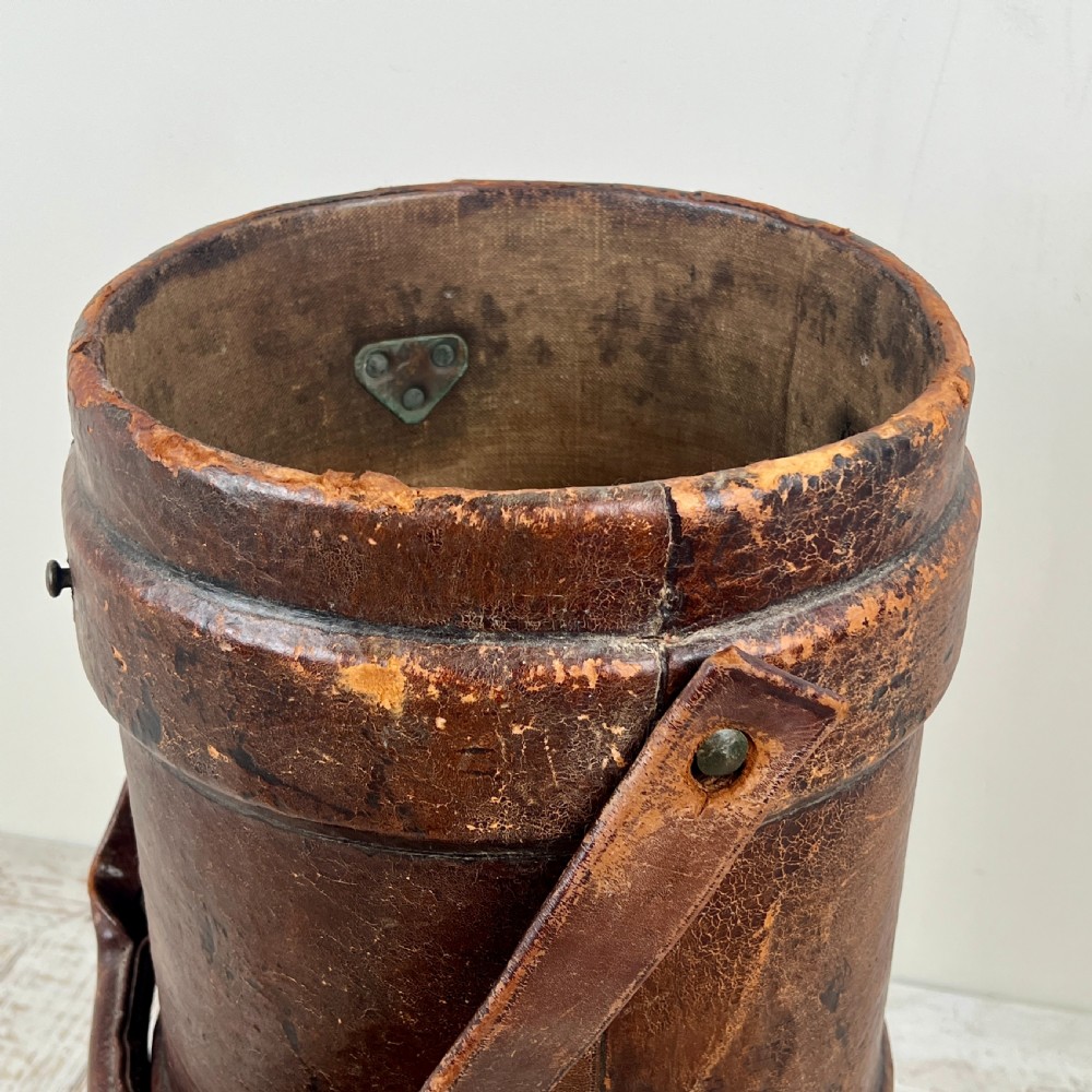 A tall cylindrical brown leather First World War artillery shell carrier featuring heavy stitched seams and a riveted side handle. View IV