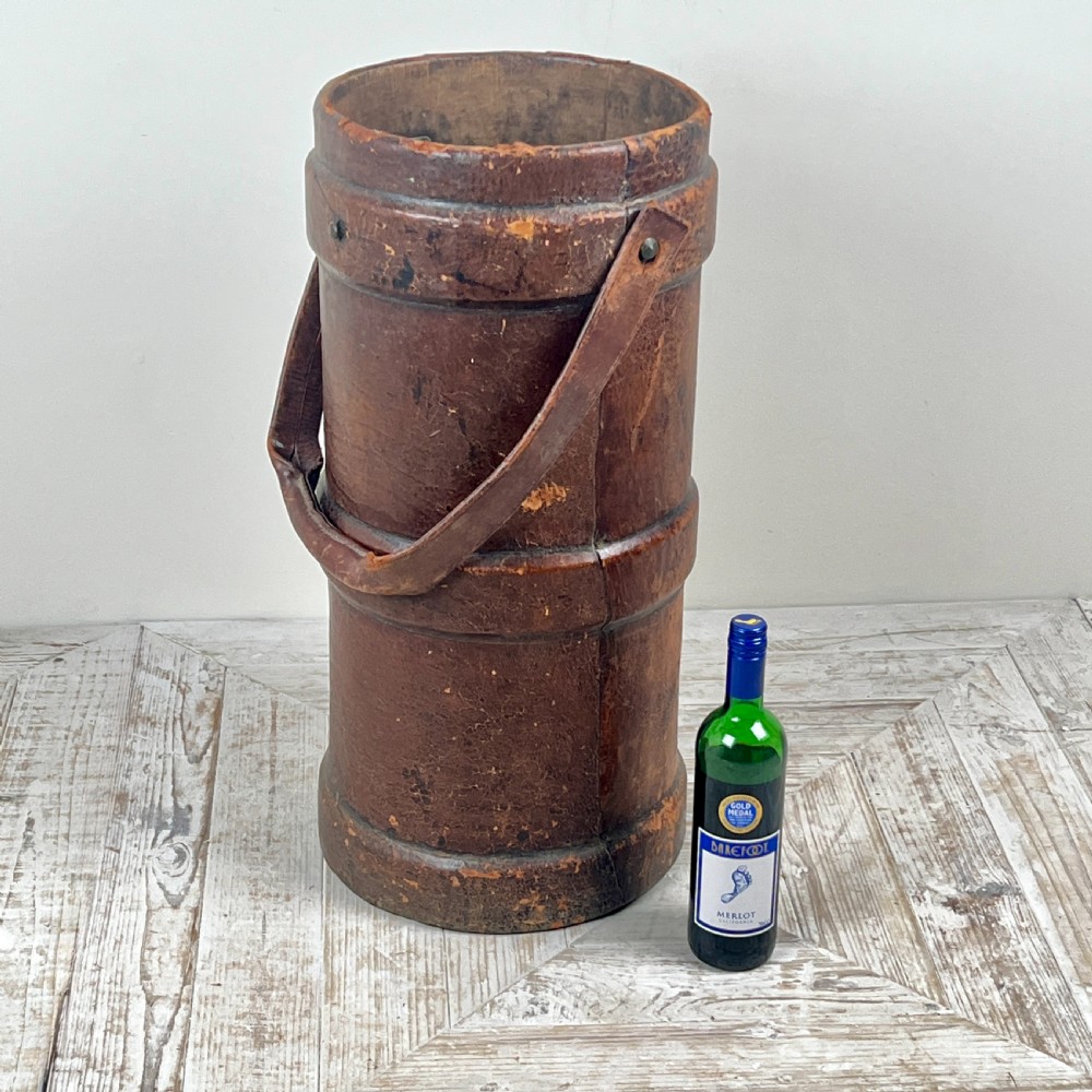 A tall cylindrical brown leather First World War artillery shell carrier featuring heavy stitched seams and a riveted side handle. View V