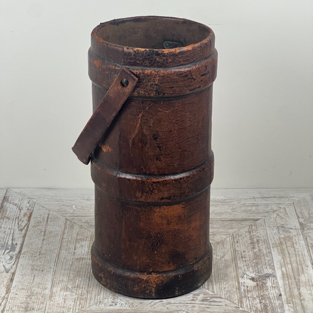 A tall cylindrical brown leather First World War artillery shell carrier featuring heavy stitched seams and a riveted side handle. View VI