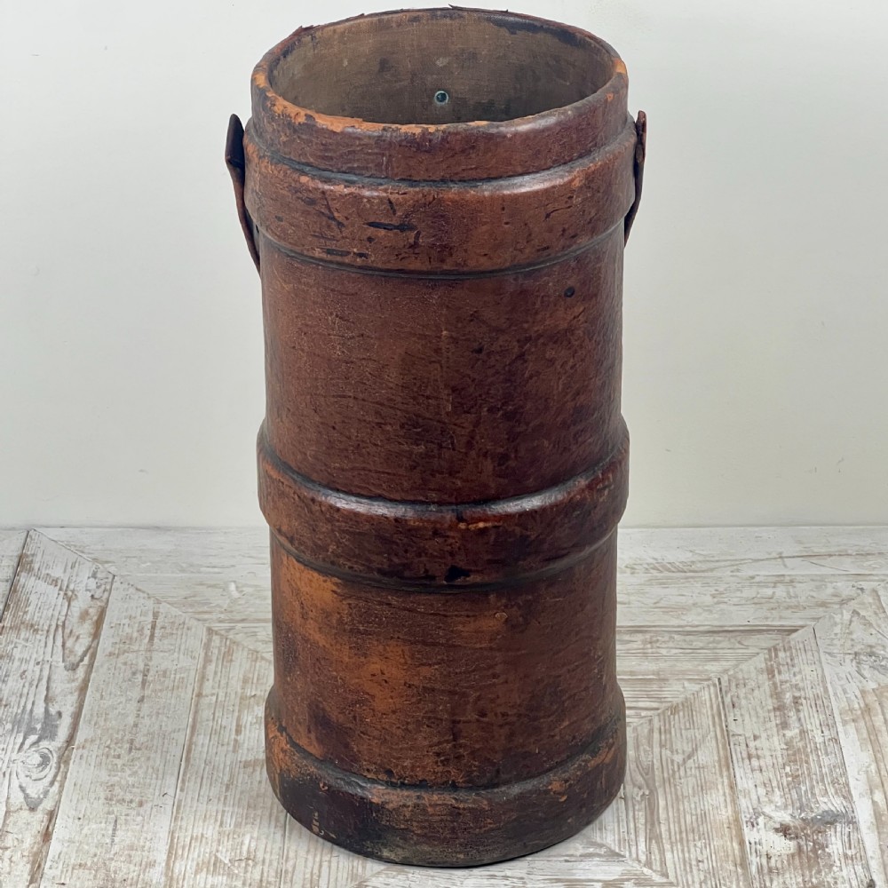 A tall cylindrical brown leather First World War artillery shell carrier featuring heavy stitched seams and a riveted side handle. View VII