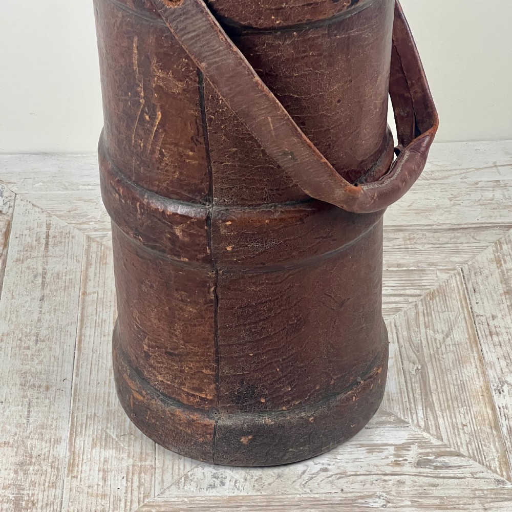 A tall cylindrical brown leather First World War artillery shell carrier featuring heavy stitched seams and a riveted side handle. View VIII