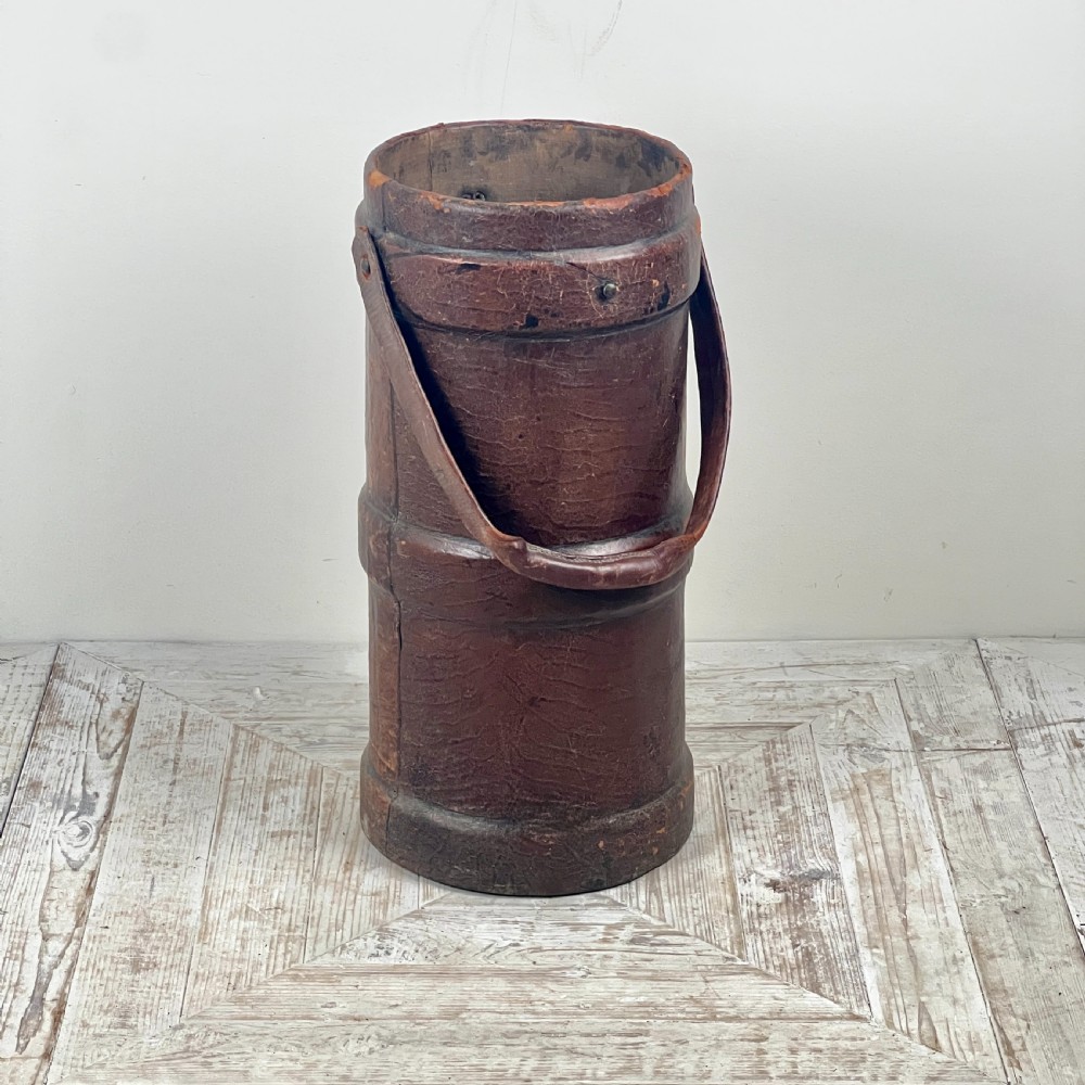 A tall cylindrical brown leather First World War artillery shell carrier featuring heavy stitched seams and a riveted side handle. View IX