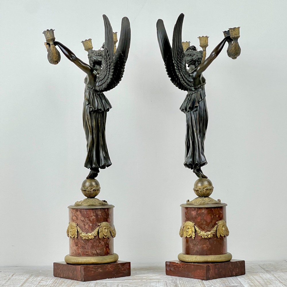 A pair of French Empire patinated bronze candelabra depicting winged victory figures standing on spheres atop rouge marble plinths with gilt bronze mounts. View II