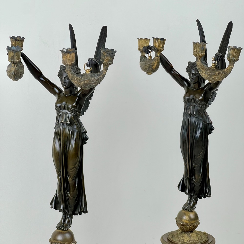 A pair of French Empire patinated bronze candelabra depicting winged victory figures standing on spheres atop rouge marble plinths with gilt bronze mounts. View III
