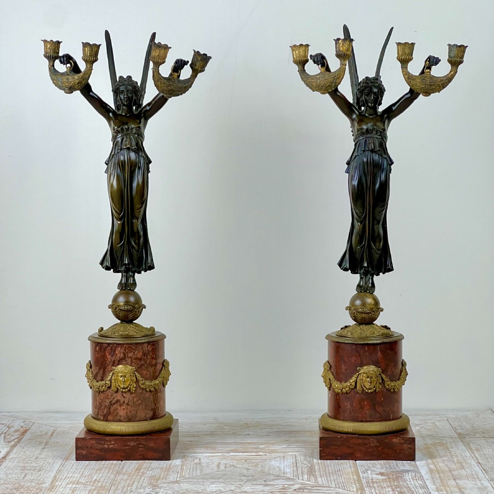 A pair of French Empire patinated bronze candelabra depicting winged victory figures standing on spheres atop rouge marble plinths with gilt bronze mounts. View IV