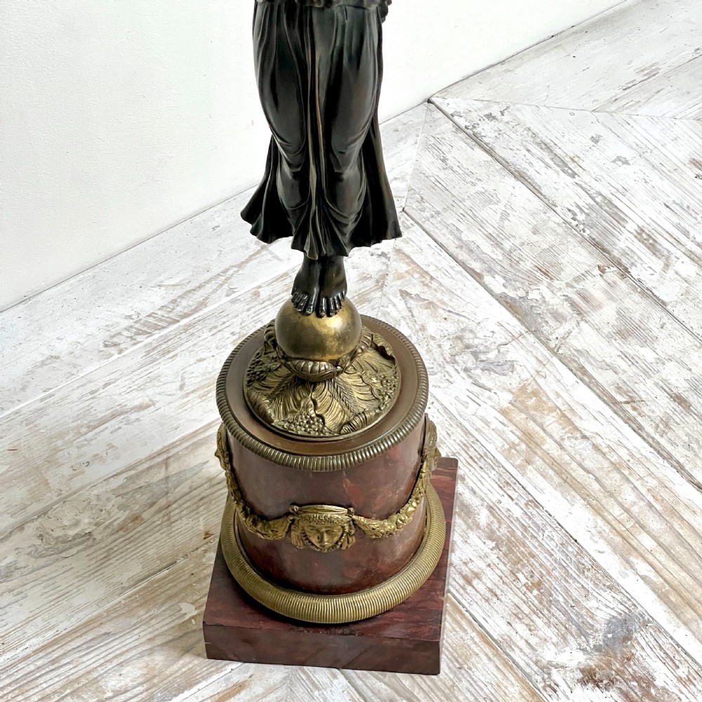 A pair of French Empire patinated bronze candelabra depicting winged victory figures standing on spheres atop rouge marble plinths with gilt bronze mounts. View V