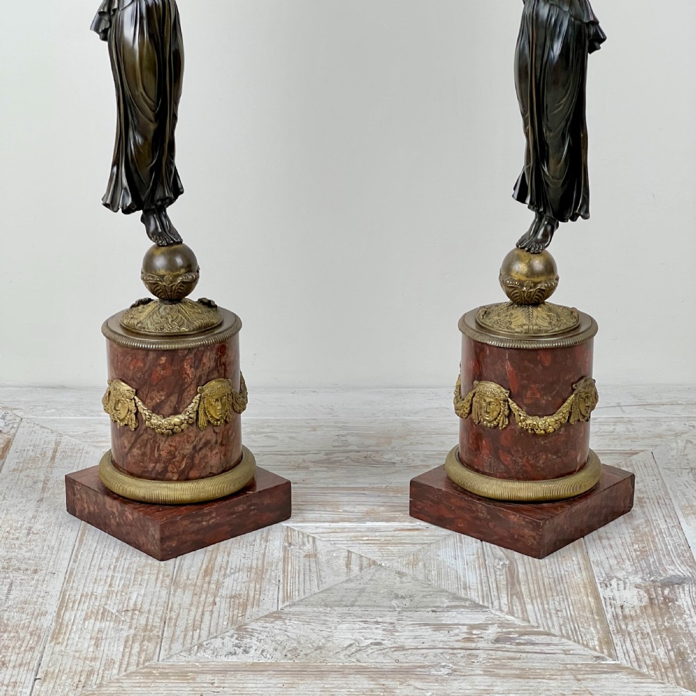 A pair of French Empire patinated bronze candelabra depicting winged victory figures standing on spheres atop rouge marble plinths with gilt bronze mounts. View VII