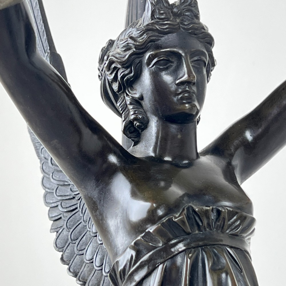 A pair of French Empire patinated bronze candelabra depicting winged victory figures standing on spheres atop rouge marble plinths with gilt bronze mounts. View VIII