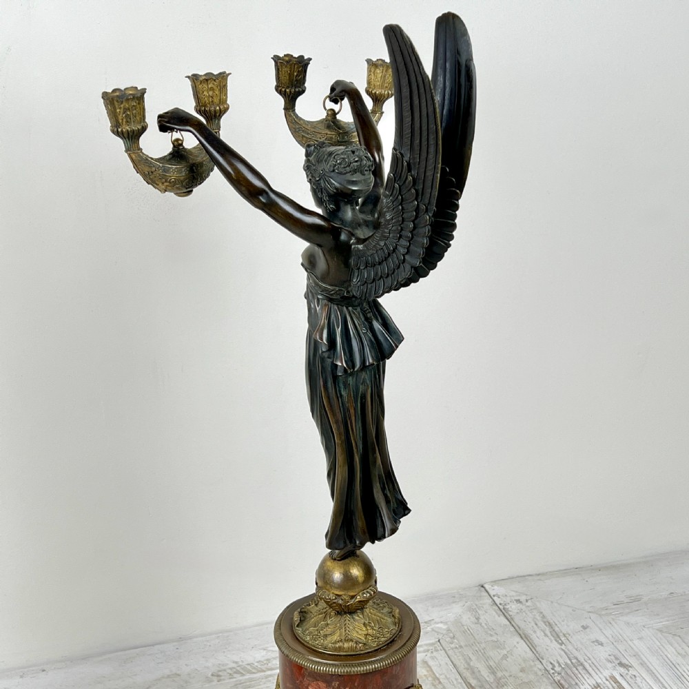 A pair of French Empire patinated bronze candelabra depicting winged victory figures standing on spheres atop rouge marble plinths with gilt bronze mounts. View X