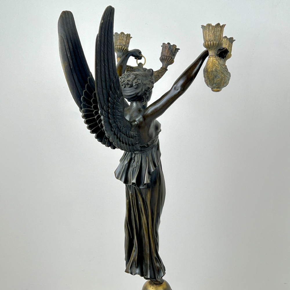 A pair of French Empire patinated bronze candelabra depicting winged victory figures standing on spheres atop rouge marble plinths with gilt bronze mounts. View XI