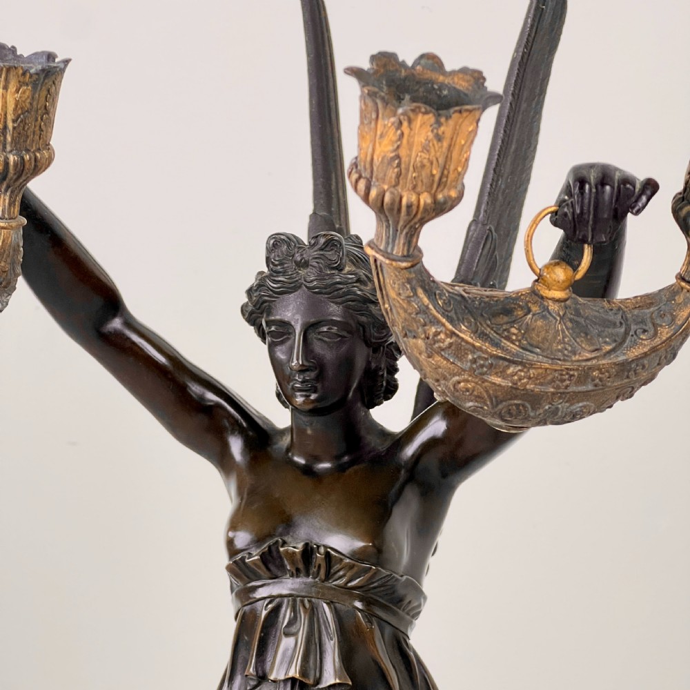 A pair of French Empire patinated bronze candelabra depicting winged victory figures standing on spheres atop rouge marble plinths with gilt bronze mounts. View XIII
