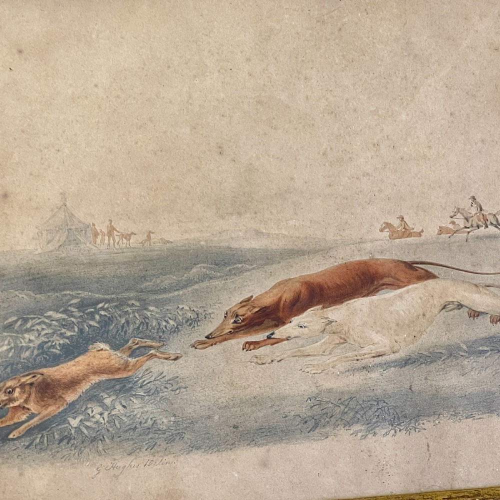 A 19th-century watercolour painting depicting two greyhounds pursuing a hare across a field, housed in a wide, ornate gilt frame with acanthus corner details. View V
