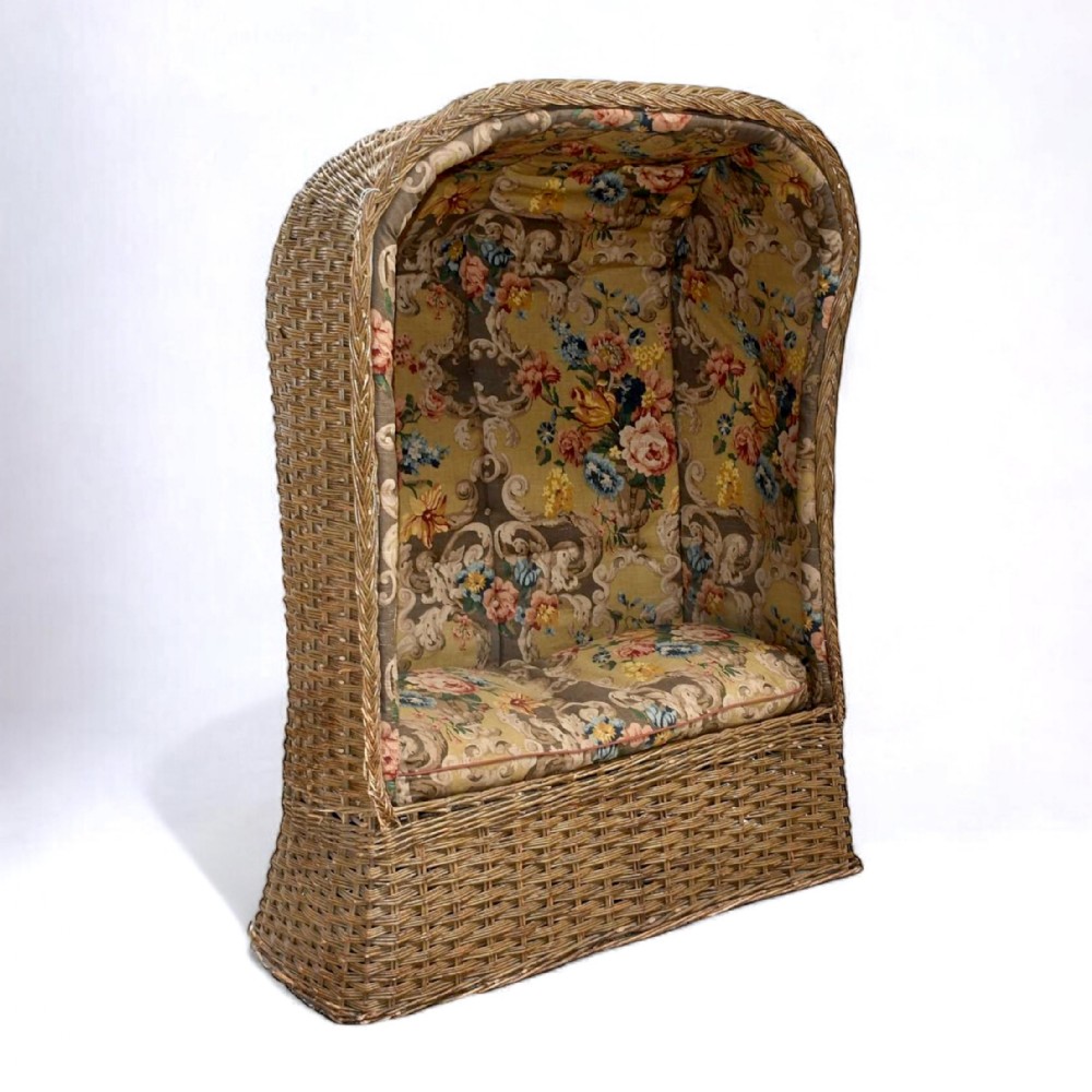 A high-backed woven wicker porters chair featuring a hooded canopy and floral upholstered linen interior.