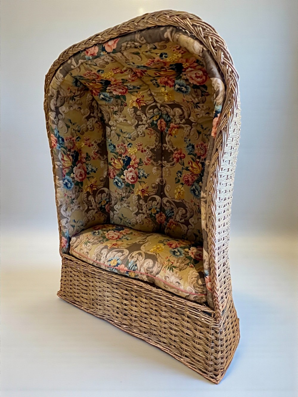 A high-backed woven wicker porters chair featuring a hooded canopy and floral upholstered linen interior. View IV
