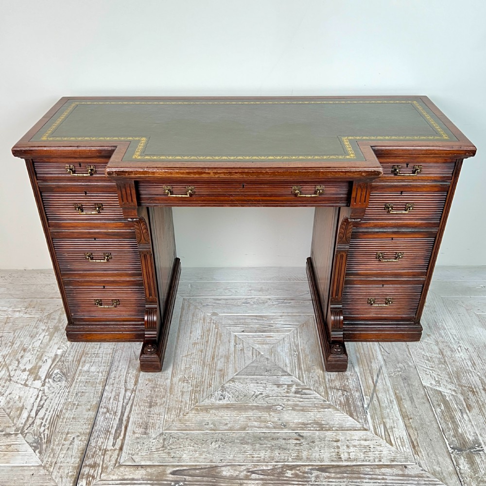 A Victorian mahogany breakfront pedestal desk featuring a green leather inset writing surface with gold tooling and multiple drawers with brass handles.