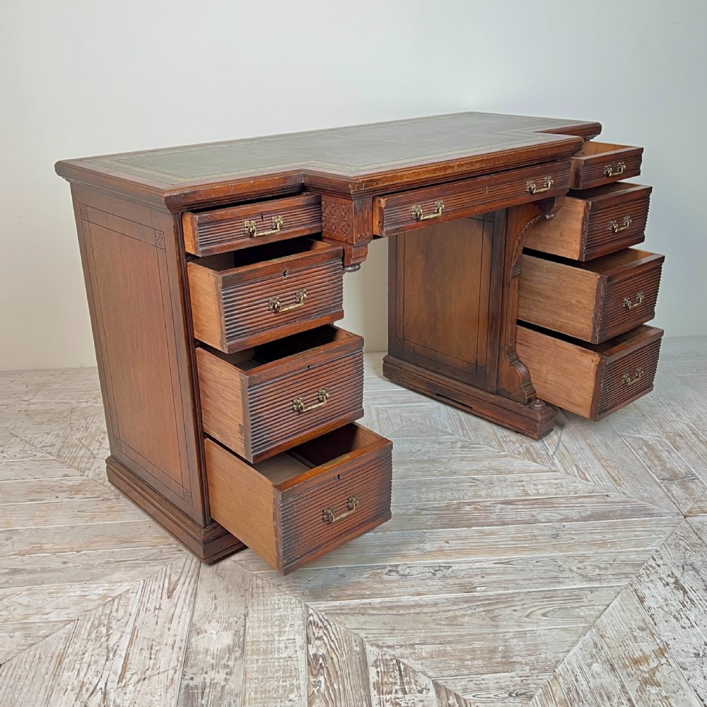 A Victorian mahogany breakfront pedestal desk featuring a green leather inset writing surface with gold tooling and multiple drawers with brass handles. View III