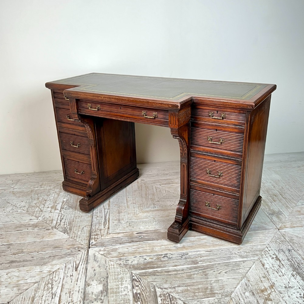 A Victorian mahogany breakfront pedestal desk featuring a green leather inset writing surface with gold tooling and multiple drawers with brass handles. View IV