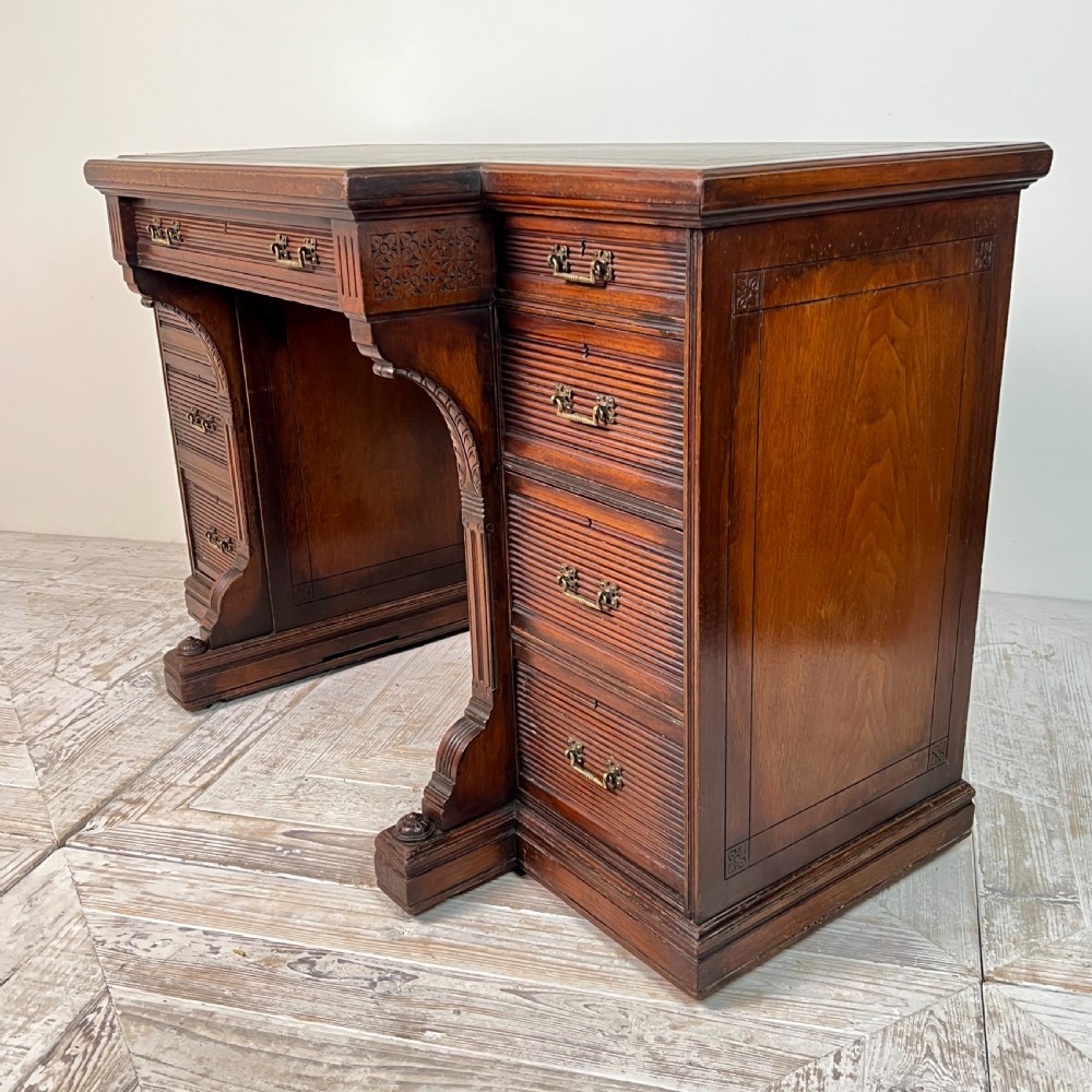 A Victorian mahogany breakfront pedestal desk featuring a green leather inset writing surface with gold tooling and multiple drawers with brass handles. View V