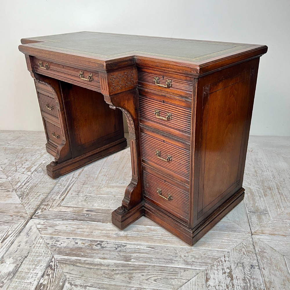 A Victorian mahogany breakfront pedestal desk featuring a green leather inset writing surface with gold tooling and multiple drawers with brass handles. View VI