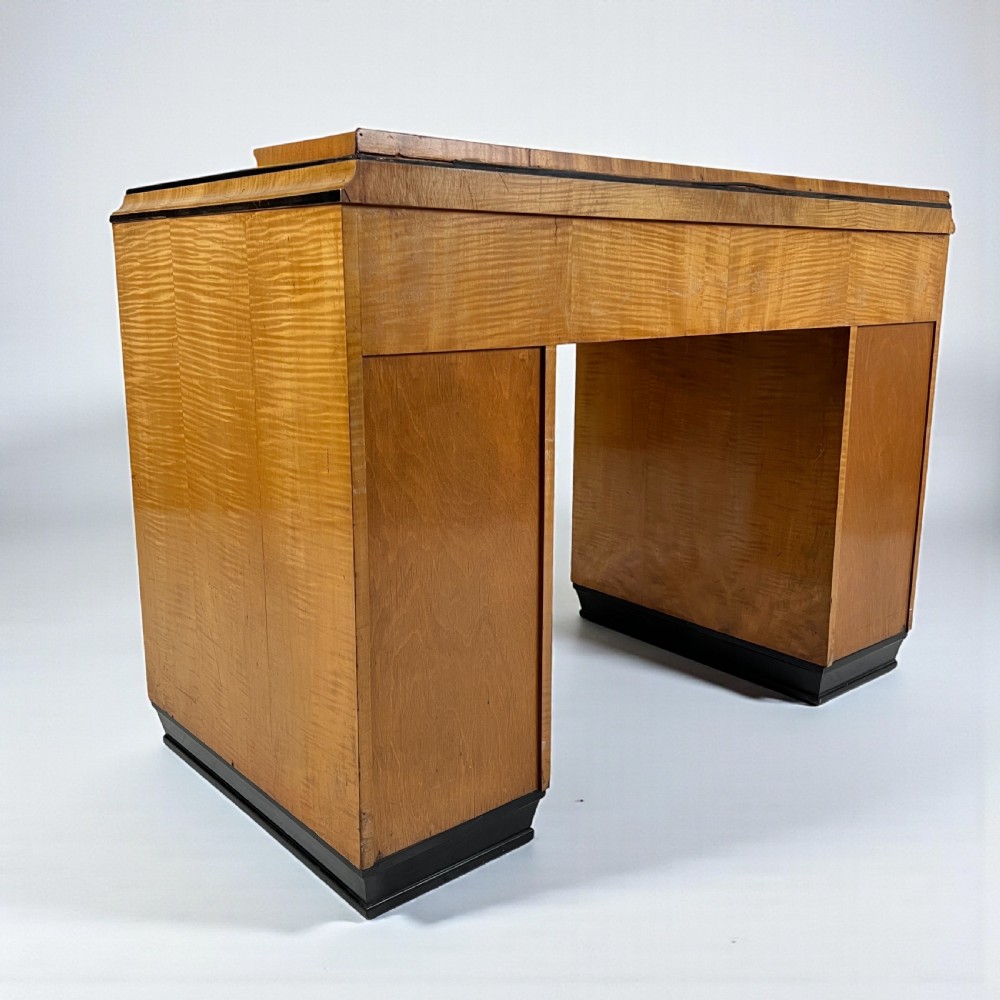An Art Deco satin birch writing desk featuring a black leather top, stepped geometric corners, dark trim, and twin pedestals with drawers. View III