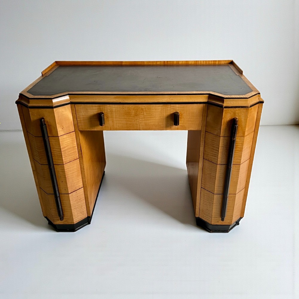 An Art Deco satin birch writing desk featuring a black leather top, stepped geometric corners, dark trim, and twin pedestals with drawers. View VI