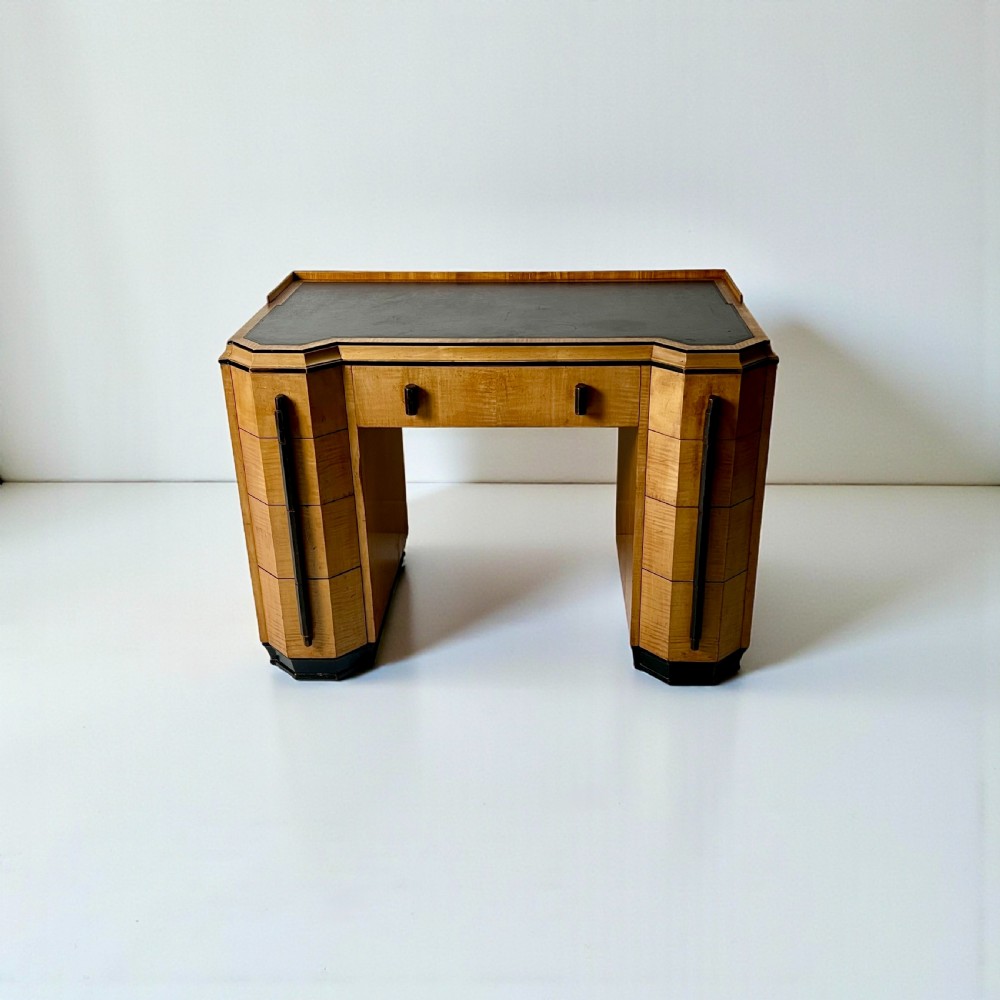 An Art Deco satin birch writing desk featuring a black leather top, stepped geometric corners, dark trim, and twin pedestals with drawers. View VII