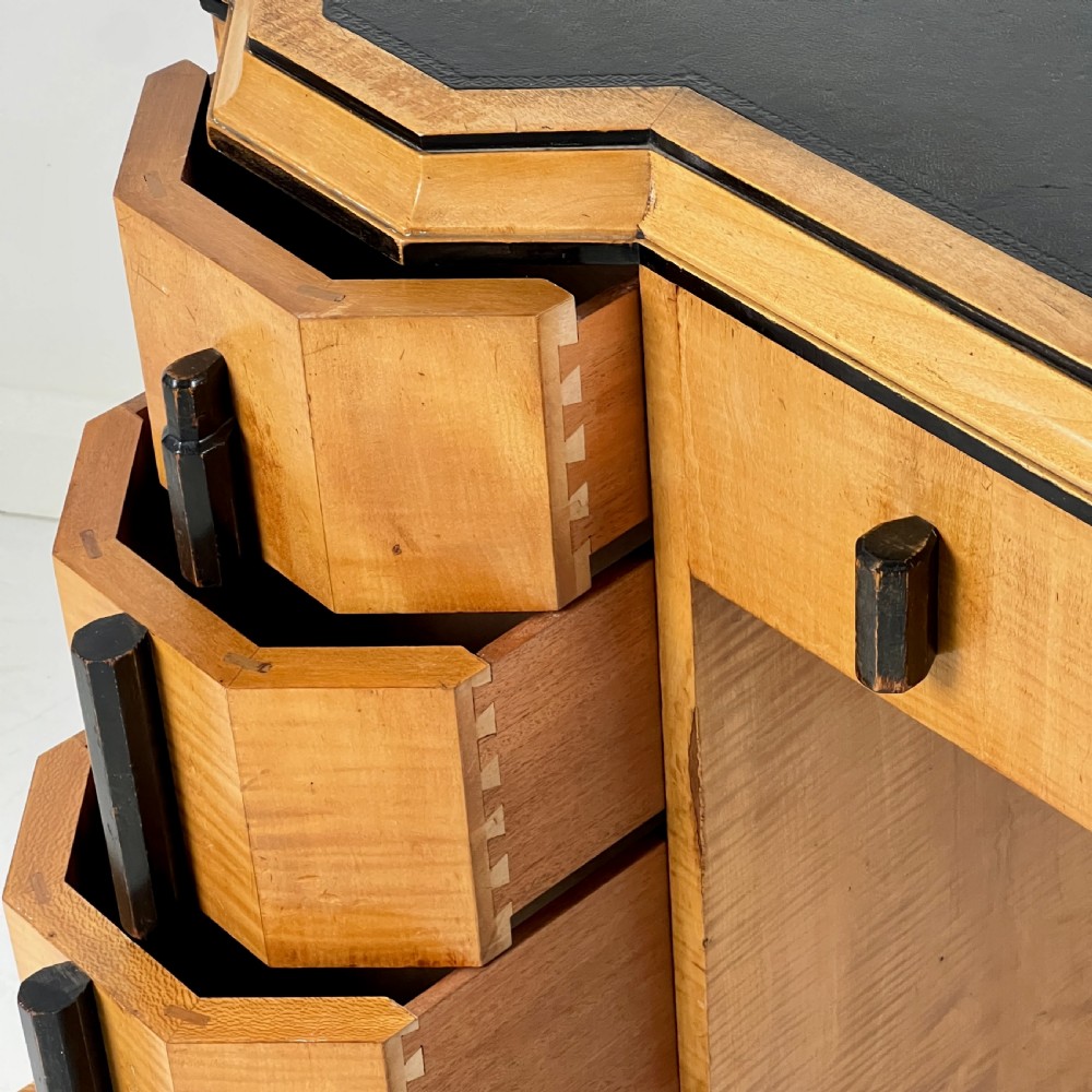 An Art Deco satin birch writing desk featuring a black leather top, stepped geometric corners, dark trim, and twin pedestals with drawers. View IX