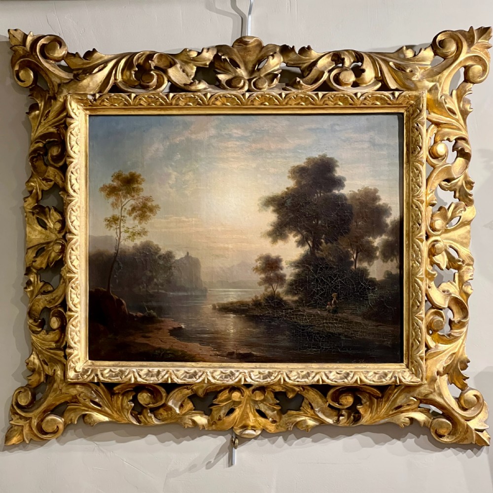 An antique oil painting on canvas depicting a tranquil riverscape framed by dense trees and a soft sky, enclosed within an ornate carved giltwood frame.