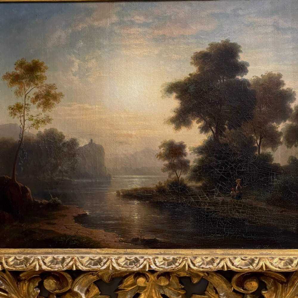 An antique oil painting on canvas depicting a tranquil riverscape framed by dense trees and a soft sky, enclosed within an ornate carved giltwood frame. View II