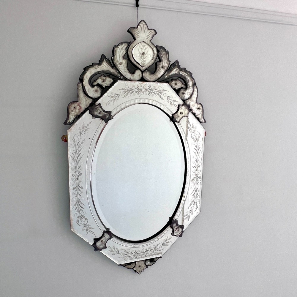 An octagonal Venetian-style wall mirror featuring etched floral borders, an oval central plate, and a decorative scrolling glass crest.