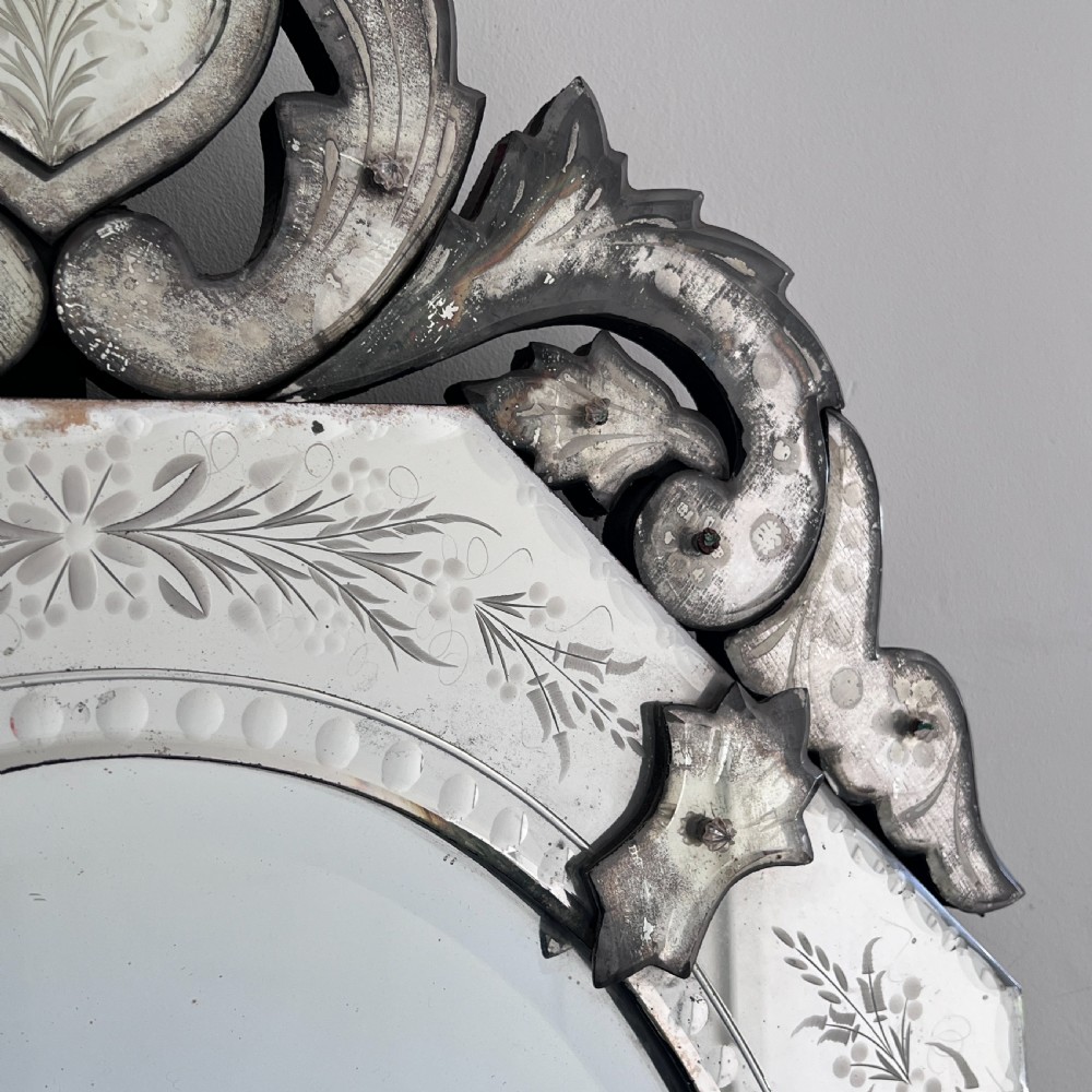 An octagonal Venetian-style wall mirror featuring etched floral borders, an oval central plate, and a decorative scrolling glass crest. View V