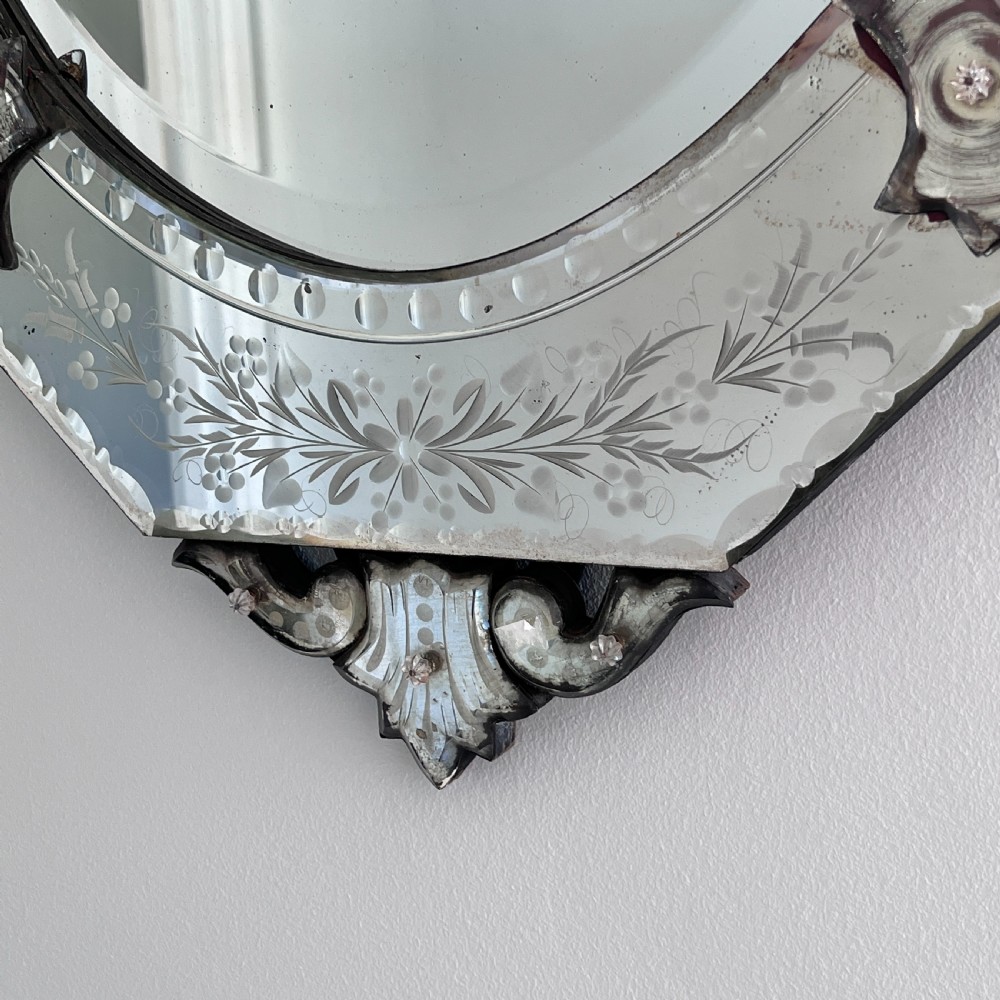 An octagonal Venetian-style wall mirror featuring etched floral borders, an oval central plate, and a decorative scrolling glass crest. View IX