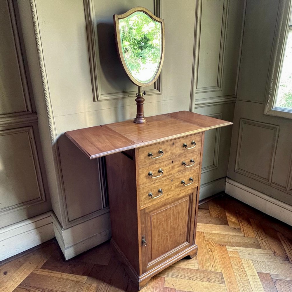 An Edwardian mahogany dressing chest featuring an adjustable shield-shaped mirror, drop-leaf top flaps, three drawers with brass handles, and a lower cupboard.