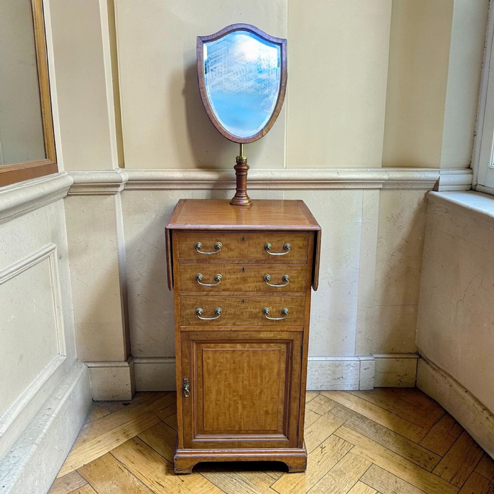 An Edwardian mahogany dressing chest featuring an adjustable shield-shaped mirror, drop-leaf top flaps, three drawers with brass handles, and a lower cupboard. View II