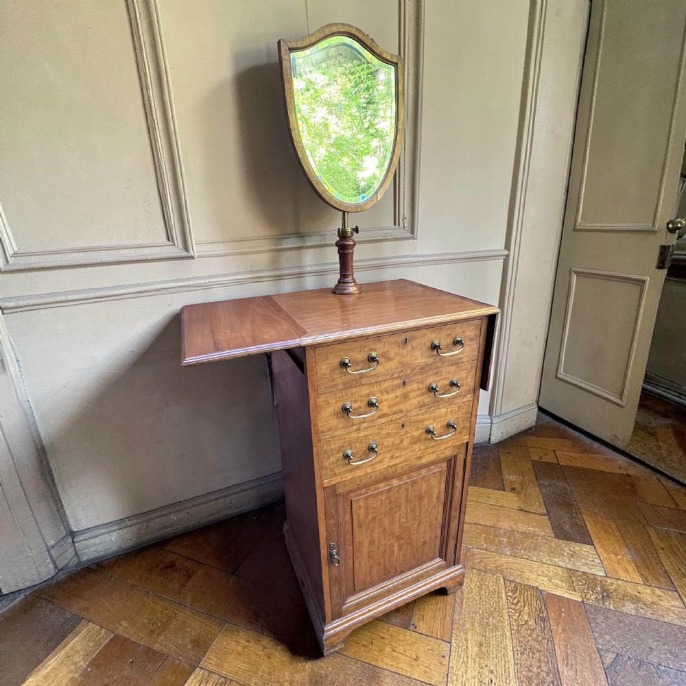 An Edwardian mahogany dressing chest featuring an adjustable shield-shaped mirror, drop-leaf top flaps, three drawers with brass handles, and a lower cupboard. View III