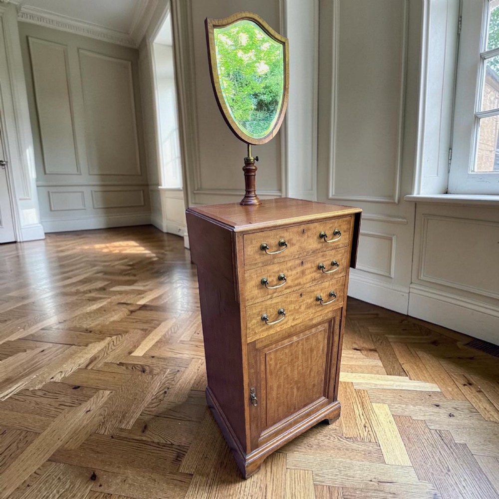 An Edwardian mahogany dressing chest featuring an adjustable shield-shaped mirror, drop-leaf top flaps, three drawers with brass handles, and a lower cupboard. View IV